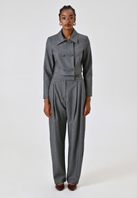 Blazer gris sur mesure avec des boutons croisés, pantalon taille haute plissé assorti et chaussures bordeaux brillantes. Texture lisse.