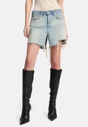 Shorts di jeans in azzurro chiaro con orlo sfilacciato e bordi sfrangiati, abbinati a stivaletti in pelle nera fino al ginocchio.