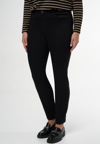 Pantalon en denim noir avec une coupe slim, comportant des poches avant et une fermeture à bouton classique. Porté avec des mocassins noirs et un haut rayé.