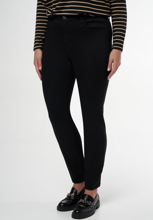 Pantalon en denim noir avec une coupe slim, comportant des poches avant et une fermeture à bouton classique. Porté avec des mocassins noirs et un haut rayé.