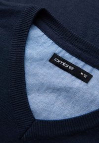 Granatowy sweter z dzianiny z jasnoniebieską wewnętrzną kołnierzykiem, z widoczną metką z brandingiem "ombre" oraz oznaczeniem rozmiaru.