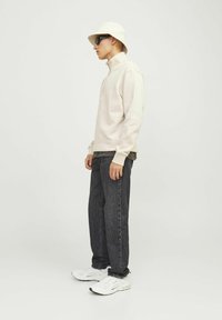 Lichtbeige zip-up sweatshirt, zwarte jeans, witte sneakers en een crèmekleurige bucket hat. Stijlvolle zonnebril maakt de casual outfit compleet.