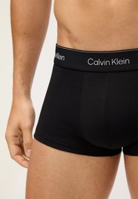 Crne pamučne bokserice s branded pojasom na kojem piše "Calvin Klein" bijelim slovima, uskog kroja i jednostavnog dizajna.