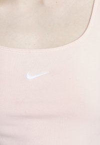 Light pink tank top featuring a round neckline and a white Nike logo embroidered on the chest. Smooth fabric with a fitted design.