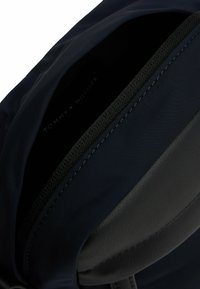 Bolsa azul marino con un exterior textil suave y una base de cuero. Cuenta con una apertura con cremallera y un interior con marca. Diseño sencillo.