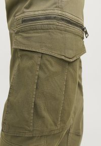 Olivové cargo nohavice so štruktúrovanou tkaninou, s vreckom na zips na stehne a vreckom s klopou nad ním, so šitými detailmi.