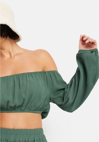 Πράσινο cropped τοπ με ανοιχτούς ώμους και μπαλονέ μανίκια, φτιαγμένο από υλικό με υφή, με εφαρμοστή μέση και χαλαρή σιλουέτα.