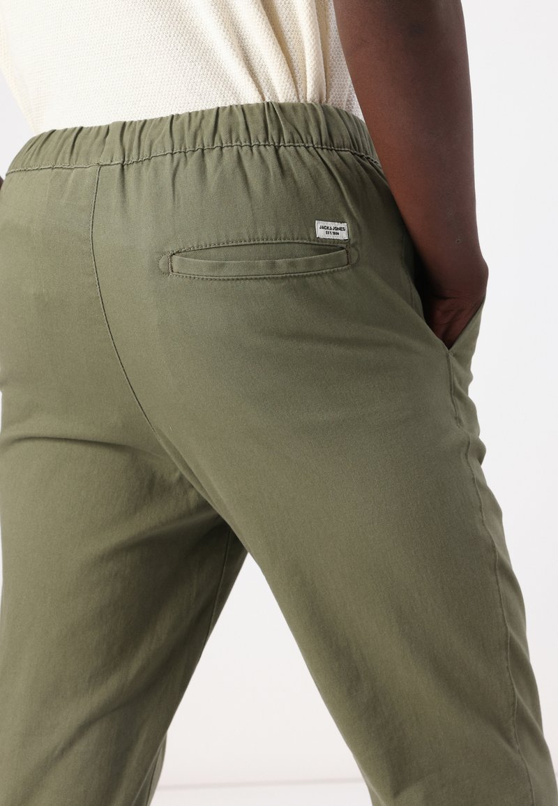 Pantalones color verde oliva con cintura elástica, bolsillos laterales y un bolsillo trasero. La tela parece ser suave y ligera con una textura lisa.