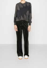 Pantaloni in velluto nero con vita regolabile, abbinati a una felpa grigia scura con un sottile motivo tie-dye. Calzature bianche visibili.