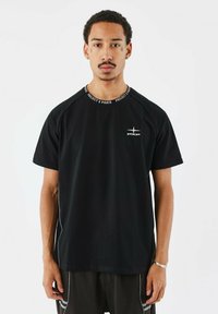 Camiseta negra de manga corta con diseño de raglán, que presenta un cuello redondo con el texto "PROJECT X PARIS" y un logo en el pecho. Acabado de tela suave.