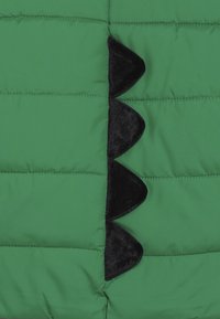Giacca a giacca verde con una texture nera a scallop al centro, con sezioni cucite visibili nel tessuto.