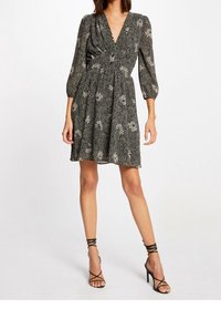 Black dress with long sleeves, v-neckline, and floral pattern. Gathered waist, flowing skirt, paired with black strappy high-heeled sandals.