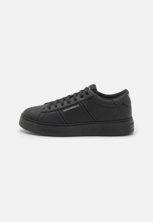 Baskets basses noires avec lacets à l’avant, semelle texturée et logo "Emporio Armani" sur le côté et la languette du talon.