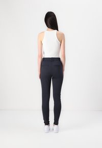 Svarta, figurnära byxor med en stretchy midja, i kombination med en vit linne. Slät textur och enkelt design, med bakfickor.