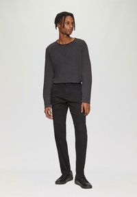 Zwarte lange mouwen shirt met een ronde halslijn en opvallende stiksels, gecombineerd met zwarte slim-fit broek en zwarte sneakers.