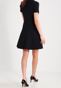 Černé šaty s krátkým rukávem a přiléhavým korzetem, rozšířenou sukní, vyrobené z hladkého materiálu; mají skrytý zip na zadní straně.