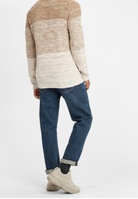 Stickad tröja i beige och ljusbrun ombre med avslappnad passform, i kombination med blå uppvikt jeans och beige sneakers.