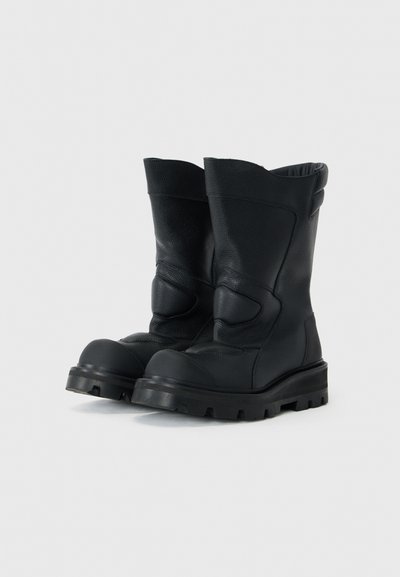 Schwarze Lederstiefeletten mit strukturiertem Finish, runder Zehenform und dicker Gummisohle mit tiefen Rillen für besseren Halt.
