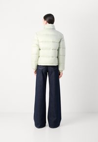 Puffig ljusgrön jacka med hög krage och elastiska manschetter, tillsammans med mörkblå vida jeans, visad bakifrån.