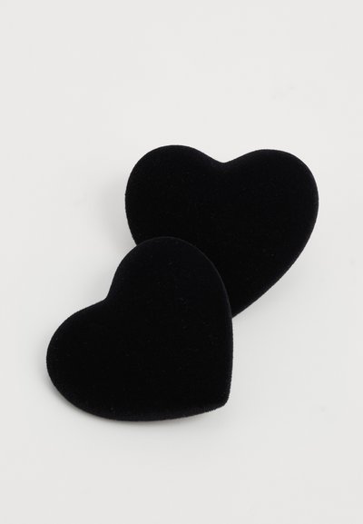 Divas divas sirds formas juvelierizstrādājumu kastes melnā samtetā uz vienkārša baltā fona, viena nedaudz pārklāj otra.