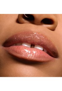 Labbra lucide di un rosa chiaro con un sottile luccichio, caratterizzate da una consistenza liscia e una forma piena. Denti naturali visibili. Accento semplice con un cerchietto argento al narice.