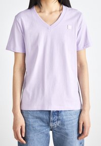 Lavendelfärgad t-shirt med V-ringning i bomull, med korta ärmar och en liten logodetalj på bröstet. Matchas med ljusblå jeans.
