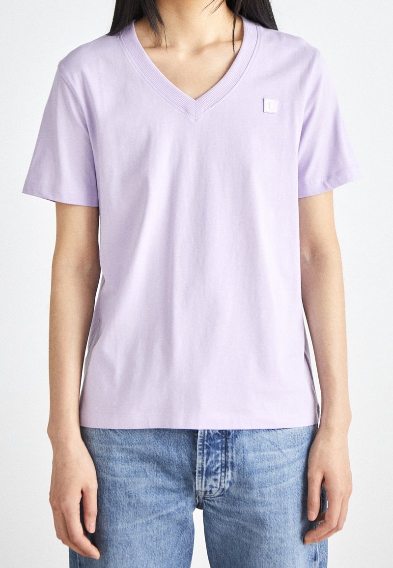 Lavendelfärgad t-shirt med V-ringning i bomull, med korta ärmar och en liten logodetalj på bröstet. Matchas med ljusblå jeans.