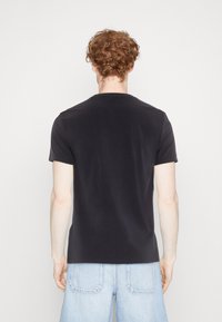 T-shirt nera a maniche corte con scollo rotondo realizzata in cotone liscio, con un design aderente e uno schienale semplice senza loghi o motivi visibili.