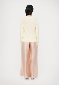 Ανοιχτό κίτρινο πλεκτό πουλόβερ με μακριά μανίκια, στρογγυλή λαιμόκοψη και ριμπ τελείωμα· συνδυασμένο με φαρδιά παντελόνια σατέν σε ανοιχτό ροζ χρώμα.