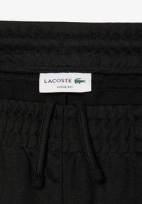 Zwarte losvallende broek van textuurstof. Heeft een elastische tailleband met een trekkoord en een wit merkembleem.