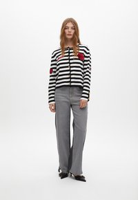 Paski czarno-biały kardigan z czerwoną haftowaną florą, złotymi guzikami, w połączeniu z szarymi spodniami typu wide-leg i czarnymi, spiczastymi butami.