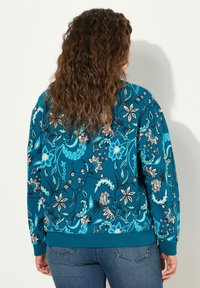 Felpa teal con motivo floreale blu e beige, scollatura arrotondata, polsini e orlo a coste. Tessuto morbido e testurizzato con maniche lunghe.