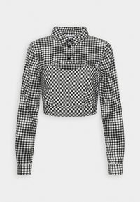 Blouse courte à carreaux vichy noir et blanc, manches longues, col boutonné et détail découpé sur la poitrine.