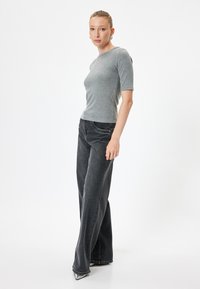 Grijs aansluitend geribbeld T-shirt met korte mouwen, gecombineerd met hoge zwarte wijde jeans. Het model draagt puntige zilveren hakken.
