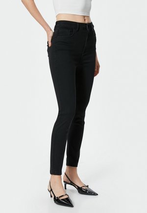 Schwarze Skinny-Jeans mit hoher Taille, ausgestattet mit Vorderentaschen und Gürtelschlaufen, kombiniert mit schwarzen Slingback-Absätzen mit spitzem Zehenbereich.