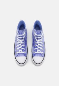 Un paio di sneakers alte in tela viola con punte e lacci bianchi su uno sfondo bianco, viste dall'alto.