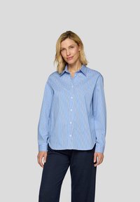 Blue and white striped button-up shirt with a collar, long sleeves, and a relaxed fit, made from a smooth fabric. Paired with dark pinstriped pants.