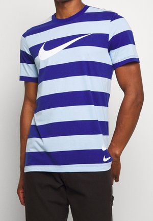 Mann trägt ein kurzärmeliges Nike T-Shirt mit blauen und hellblauen horizontalen Streifen und weißen Swoosh-Logos auf der Brust und in der Nähe des Saums.