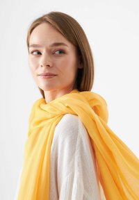 Geel chiffon sjaal gedrapeerd om de nek, met een zachte, lichte textuur en rafelige randen, in combinatie met een witte, gestructureerde top.