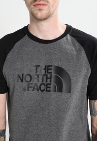 Gray and black short-sleeve T-shirt featuring a bold, black graphic logo of "The North Face" on the front. Cotton material, relaxed fit.