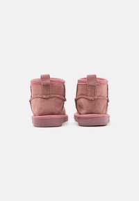 Stivali alla caviglia in suede rosa con una texture morbida, dotati di un tassello posteriore a loop, dettagli cuciti e suola in gomma tono su tono.