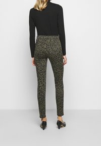 Pantalones ajustados verde oliva con un estampado de leopardo negro. Están hechos de un material suave y elástico, con bolsillos traseros y una cintura de altura media.