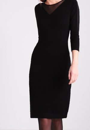 Sort kjole med en tætsiddende silhuet, der har en V-udskæring og trekvartærmer. Teksturert mønster og glat stof fremhæver designet.
