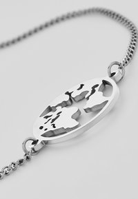 Silberarmband mit einem ovalen Anhänger, der ein durchbrochenes Weltkarte-Design zeigt. Die Kette hat eine glatte, strukturierte Oberfläche.