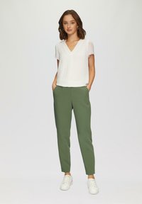 Witte blouse met korte mouwen en V-hals, gecombineerd met olijfgroene tapered broek en witte sneakers, wat zorgt voor een casual ensemble.