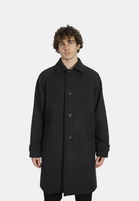 Cappotto nero a spina di pesce con colletto, cinque bottoni e maniche lunghe, caratterizzato da una vestibilità rilassata e un tessuto a trama.