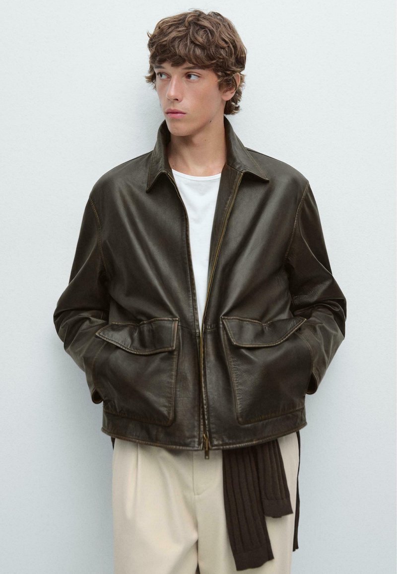 Dark brown leather jacket with a front zipper, collared neck, and two large patch pockets. Smooth texture and visible stitching details.