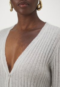 Cardigan côtelé gris clair avec un décolleté en V profond et une fermeture à boutons, mettant en valeur une texture douce et une silhouette ajustée.