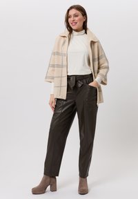 Beige plaid wool coat with a shawl collar over a cream turtleneck, paired with dark brown leather wide-leg pants and taupe heeled ankle boots.