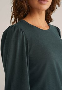 Sötétzöld, hosszú ujjú blúz kerek nyakkivágással és puffos ujjakkal, texturált anyagból, finom bordázott mintával.